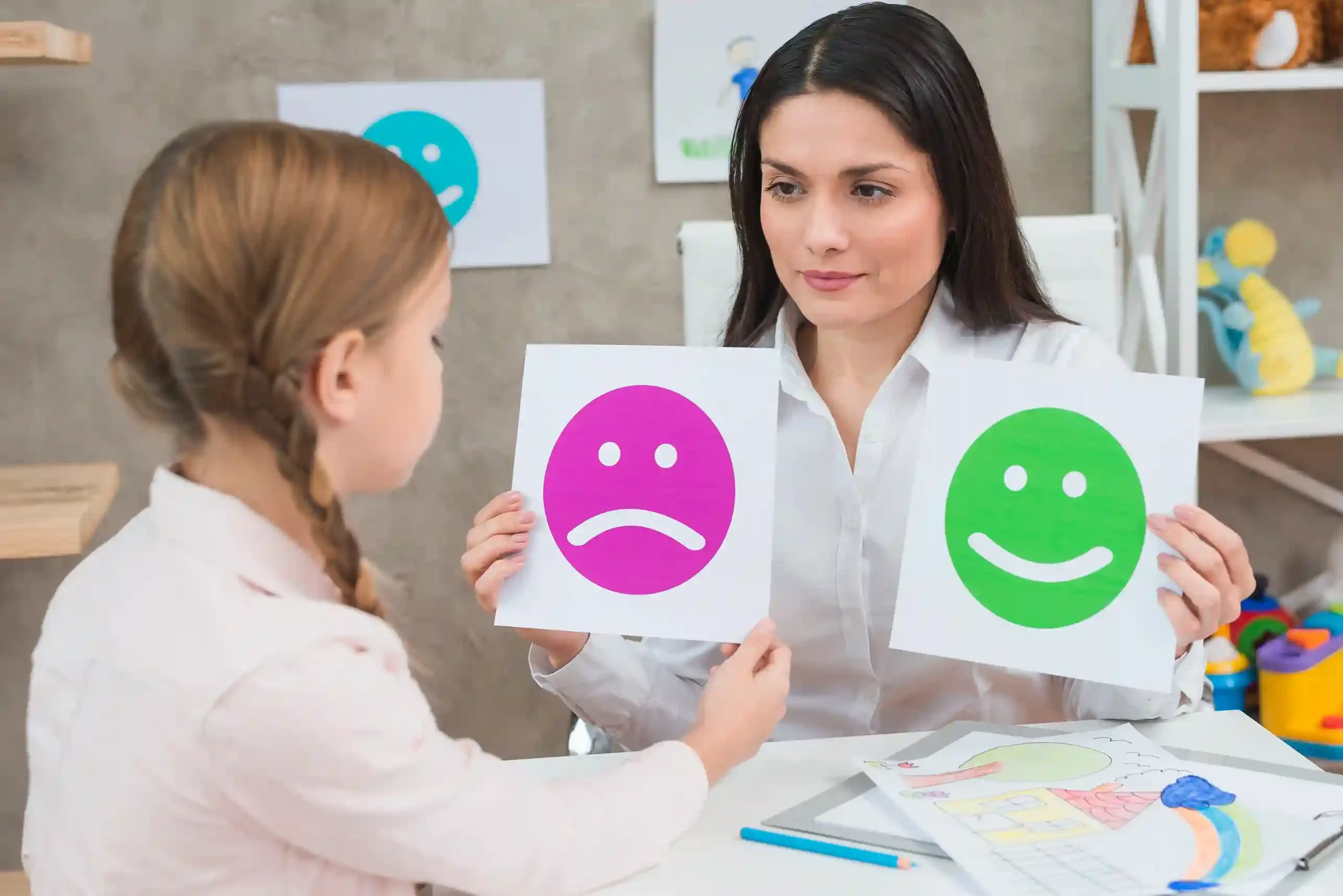 Close up girl choosing sad face emoticons paper held by smiling young psychologist